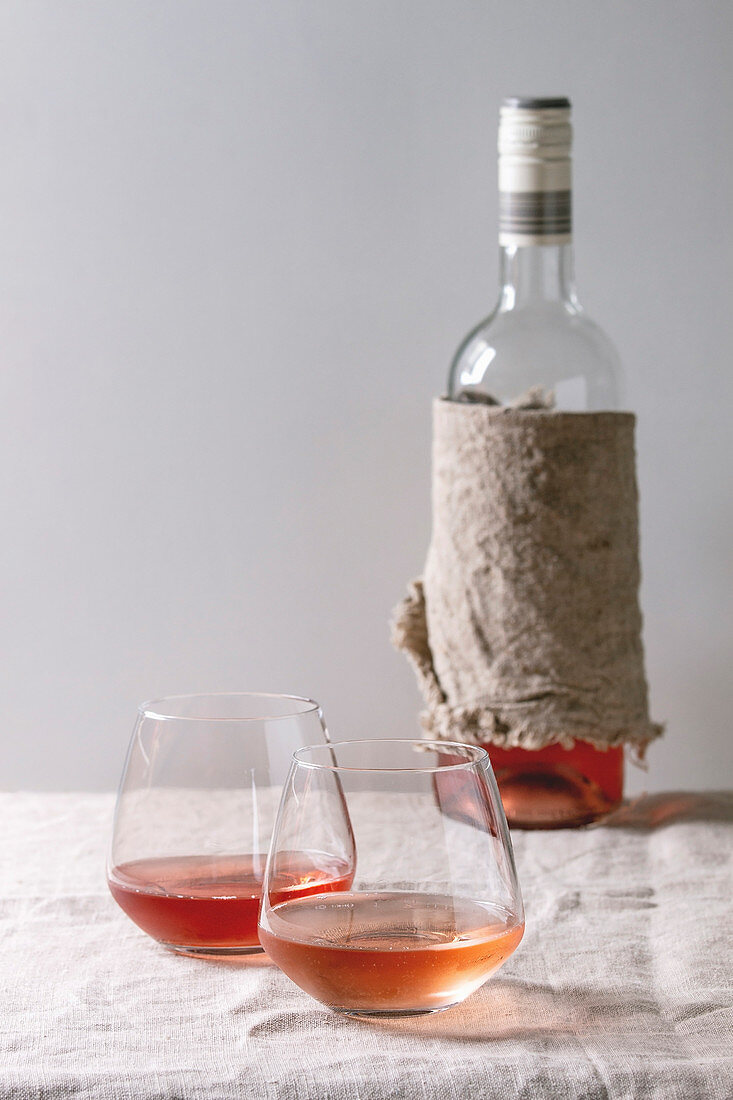 Two glasses of different rose wine standing on grey linen table cloth with bottle