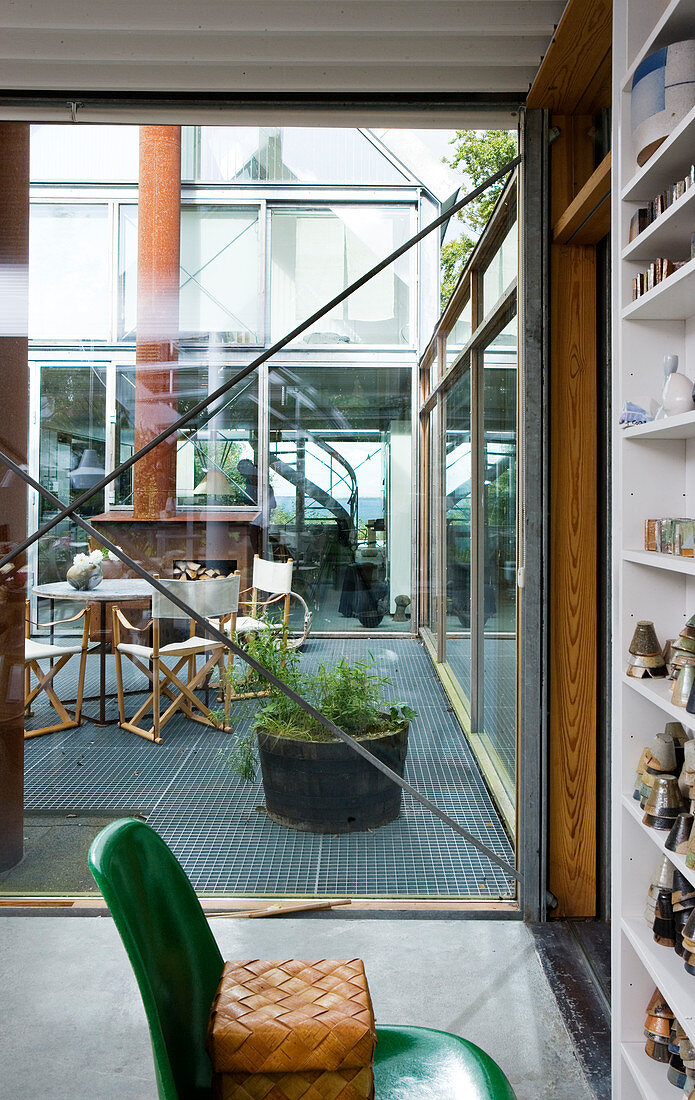 Blick durch die Fensterfront ins Atrium mit Gartenmöbeln