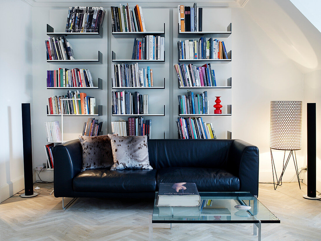 Black leather couch and glass table in front of an open wall shelf in the living room