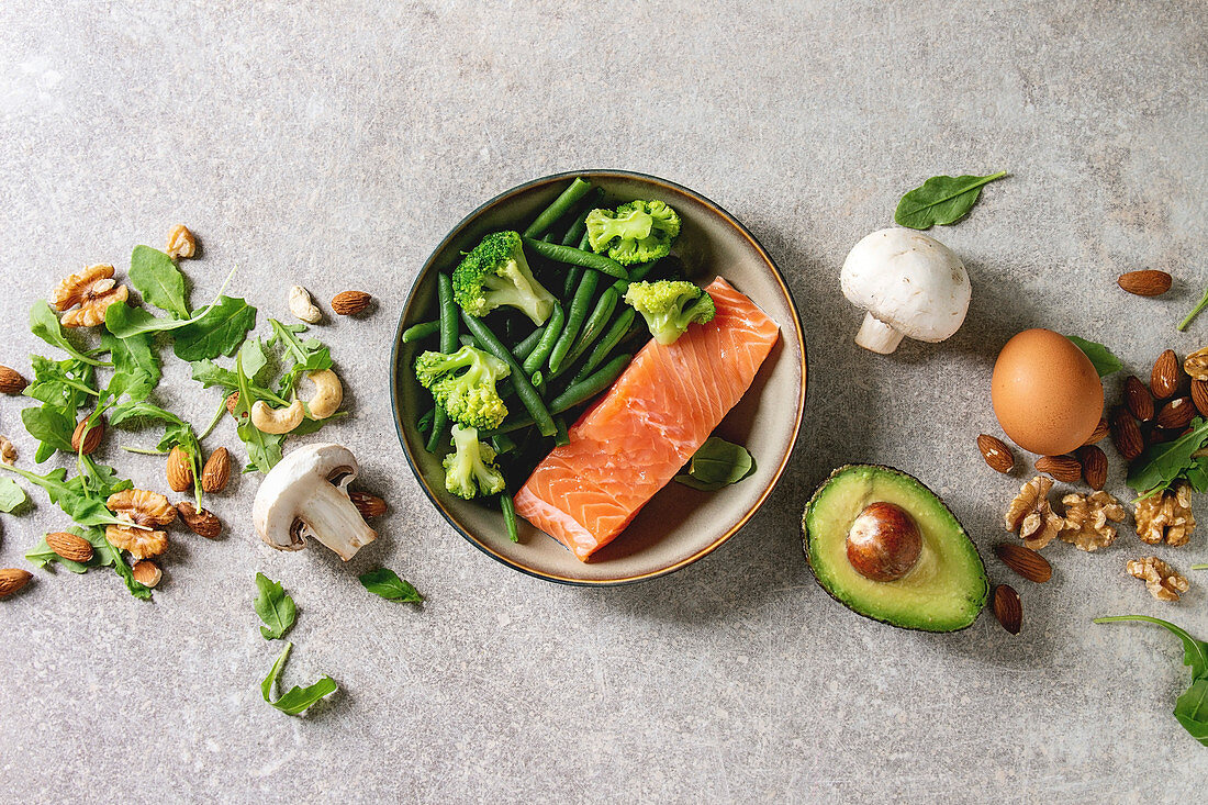 Ketogenic diet ingredients for cooking dinner. Raw salmon, avocado, broccoli, bean, olives, nuts mushrooms, eggs in ceramic bowls