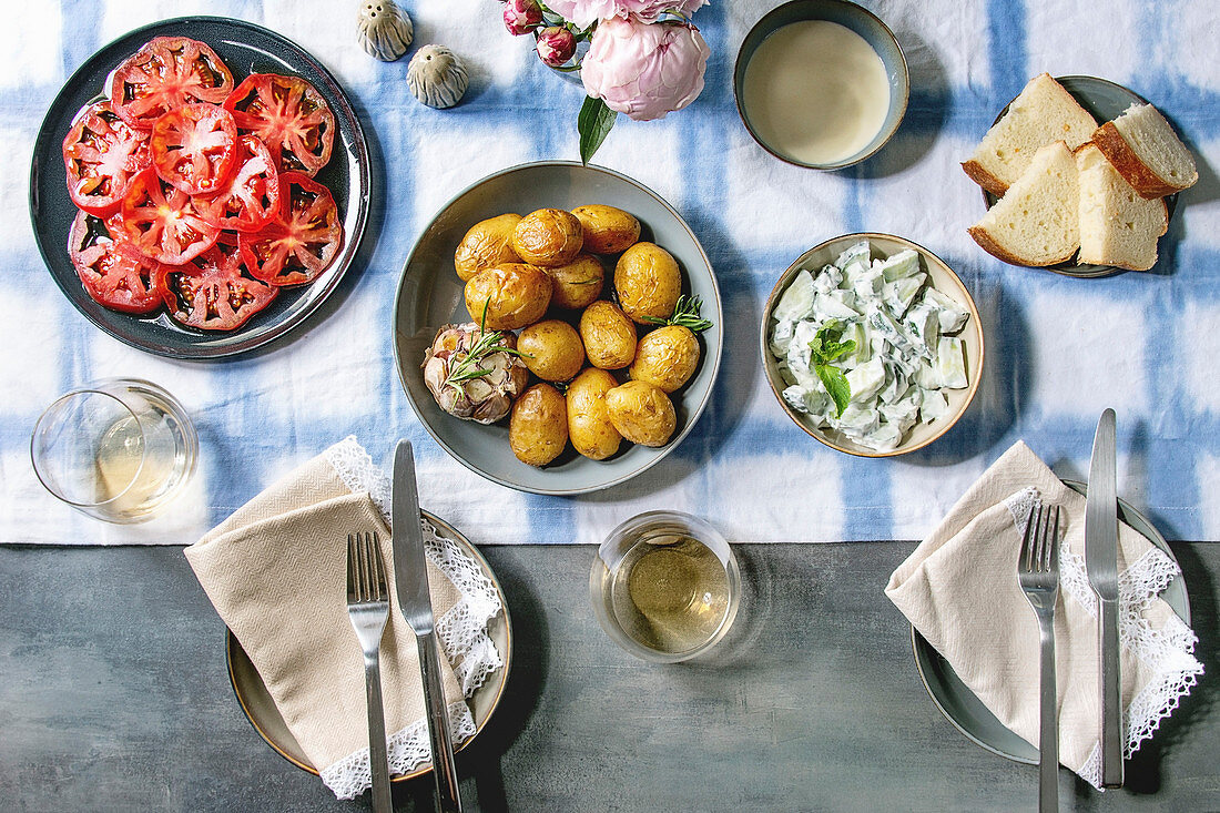 Young baked potatoes, tomato carpaccio, cucumber salad, bread, wine, sauce and flowers