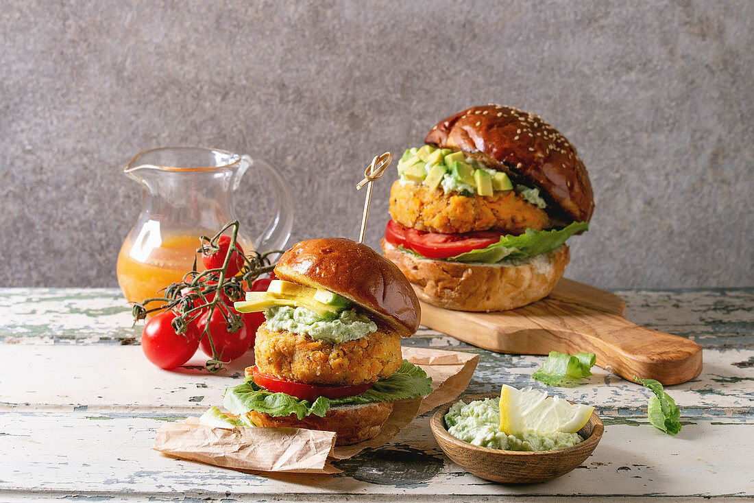 Vegan burgers with carrot and avocado in classic bun, served on wooden board with avocado sauce and ingredients