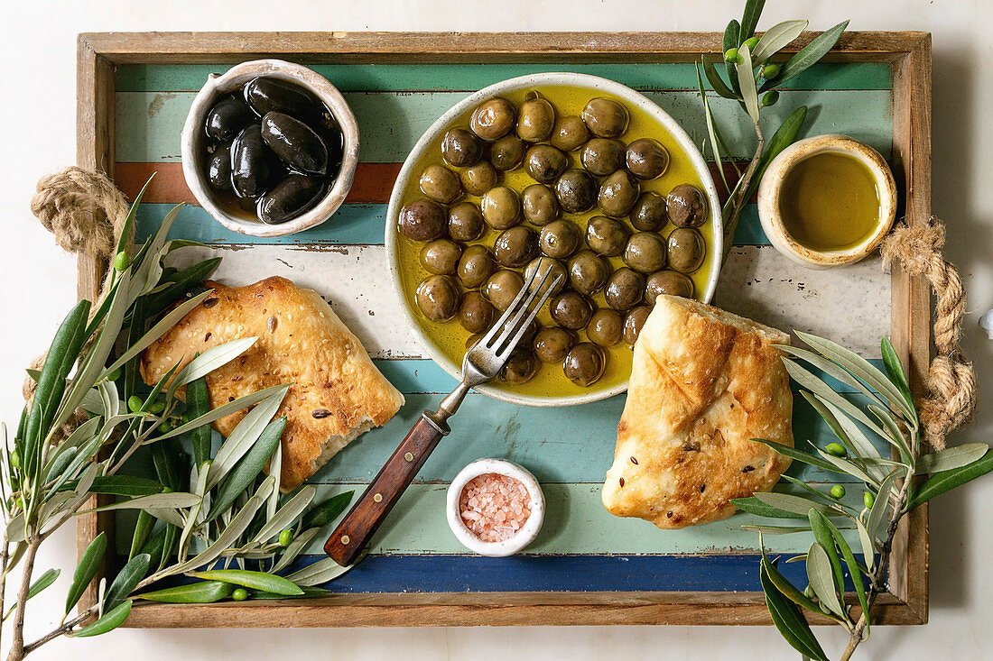 Variety of green and black whole olives in olive oil served in ceramic bowls with fresh baked ciabatta bread