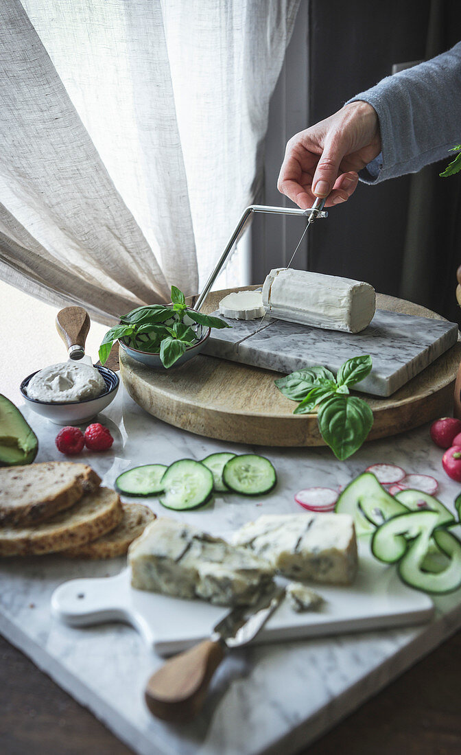 A woman slicing soft cheese on a cheese board, with various vegetables