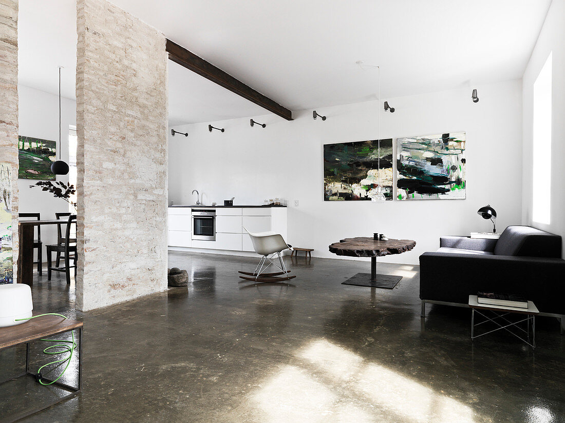 A large open-plan, loft-style living room with a concrete floor and a brick wall