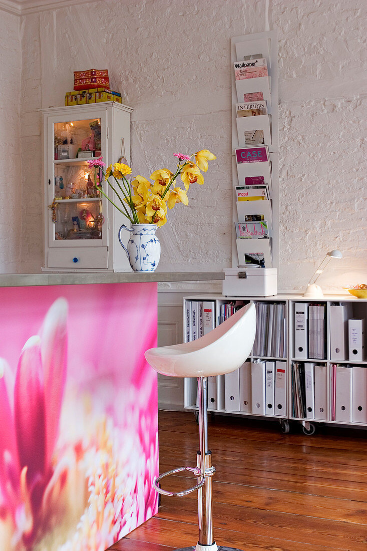 Zeitschriftenhalter und Vitrine an der Wand über einem Regal mit Ordnern