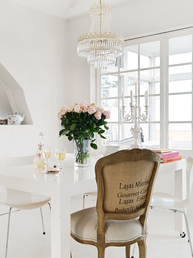 A baroque chair at a white table with a bouquet of roses under a chandelier