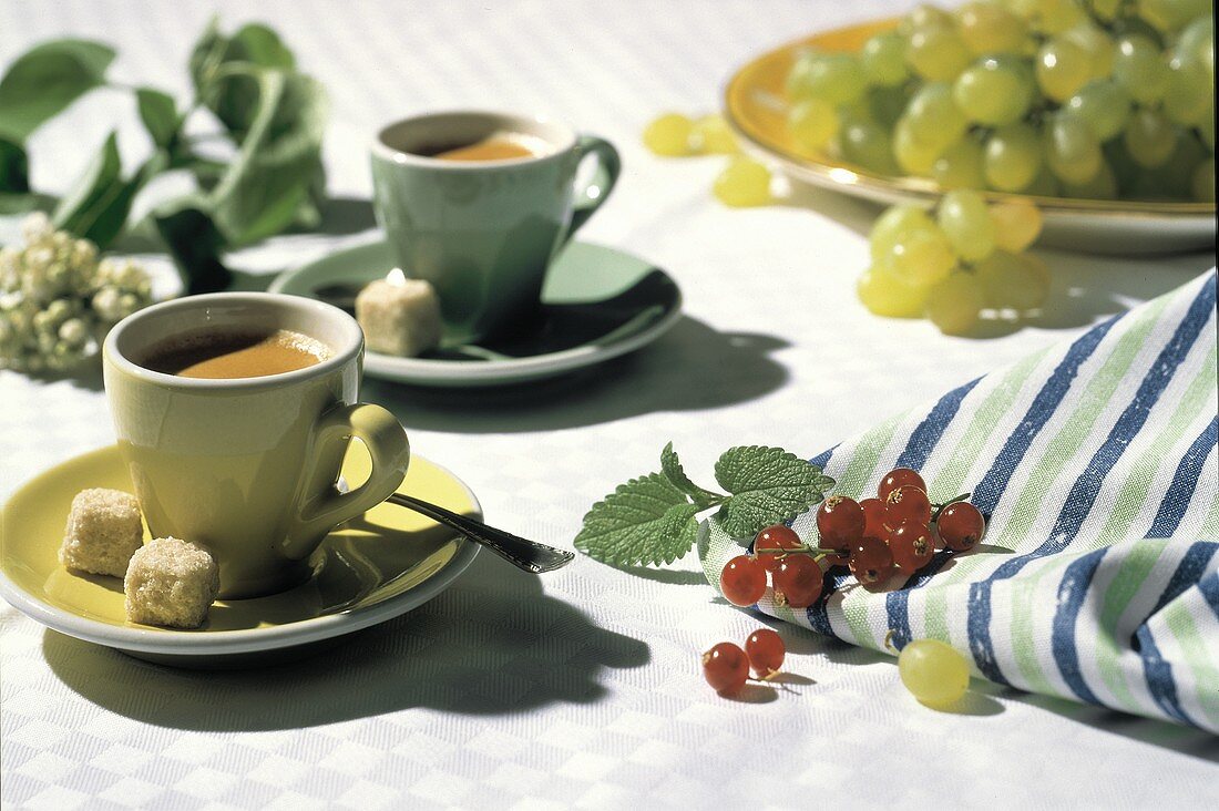 Zwei Tassen Espresso auf Tisch, Deko: Johannisbeeren, Trauben