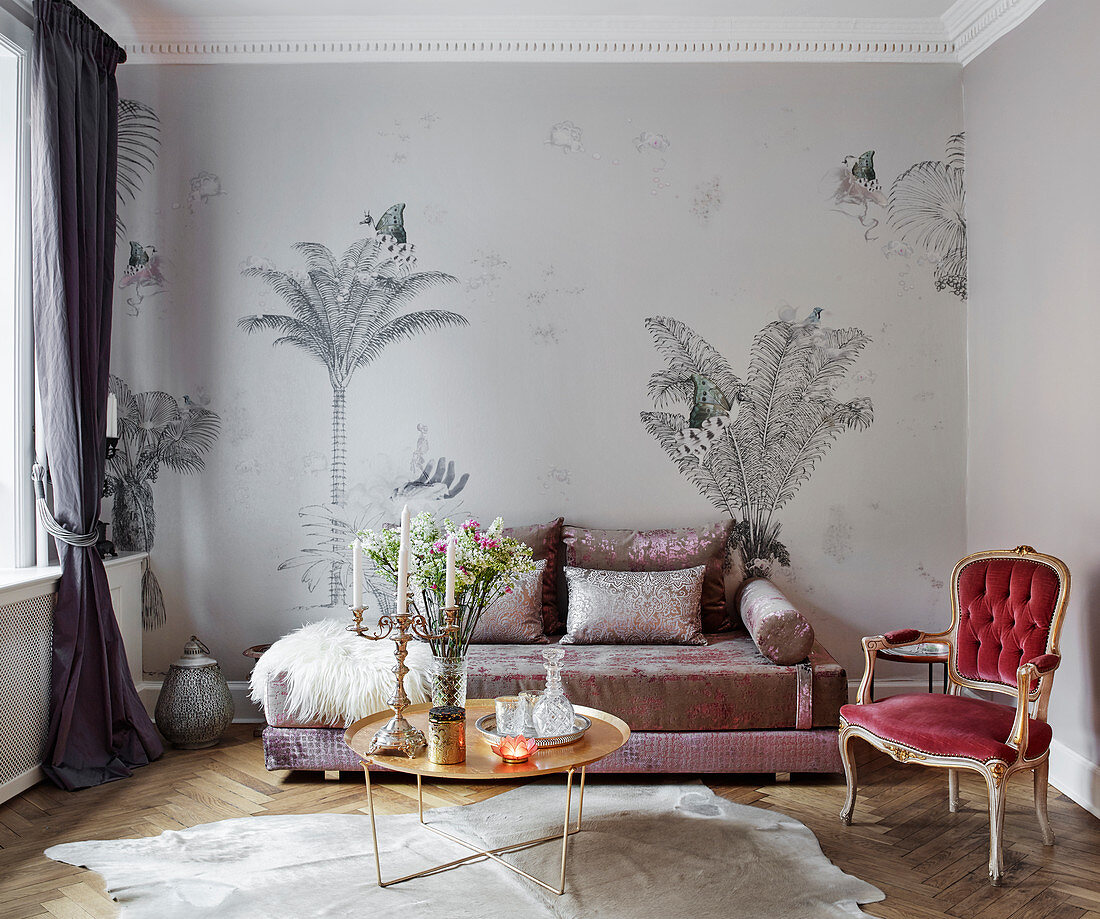 An elegant sofa in front of a wall papered with palm tree wallpaper with a coffee table and an antique chair in a living room