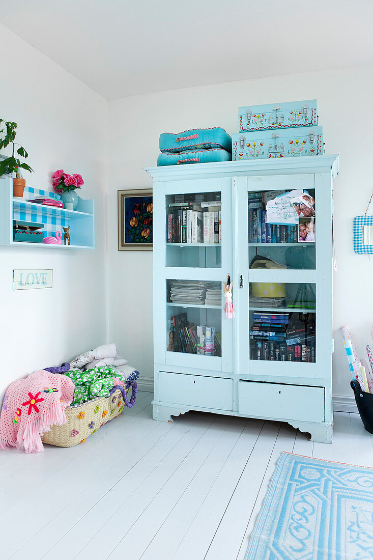 Hellblauer Vitrinenschrank mit Büchern, Sitzkissen und Köfferchen