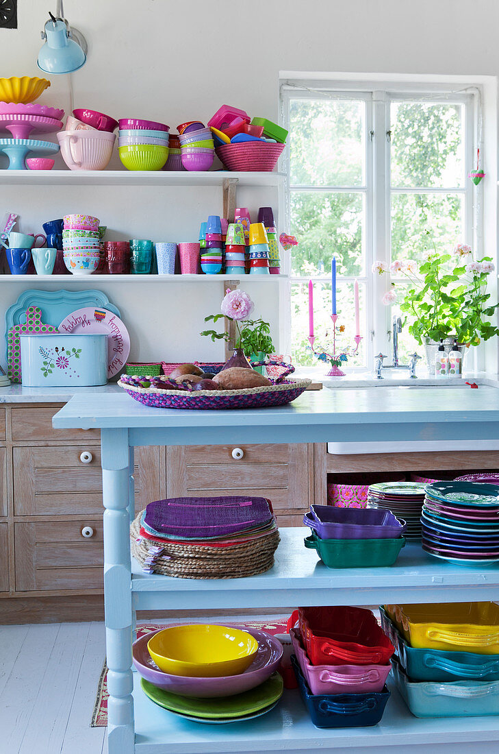 Light blue, open shelf with colorful dishes in an open plan kitchen-living room