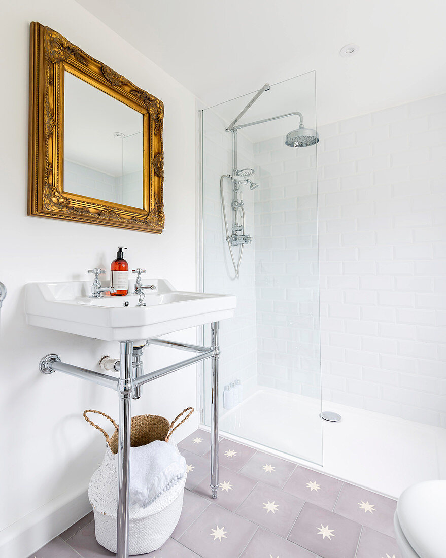 Sink below gilt-framed mirror and shower with glass screen in bathroom