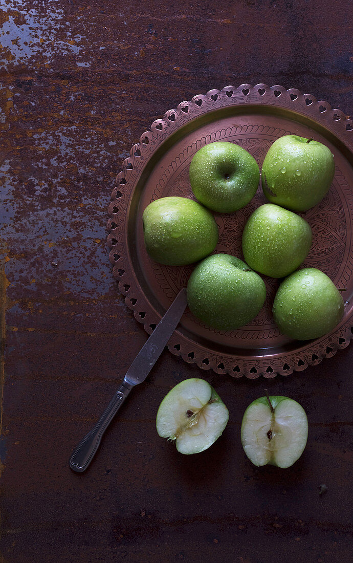 Metal knife placed near plate with fresh green apples on shabby tabletop