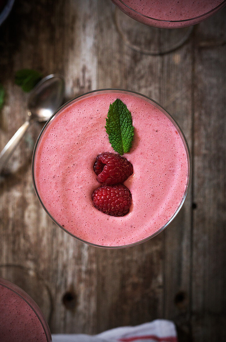 Glass of delicious pink beverage with raspberry and mint placed on wooden tabletop