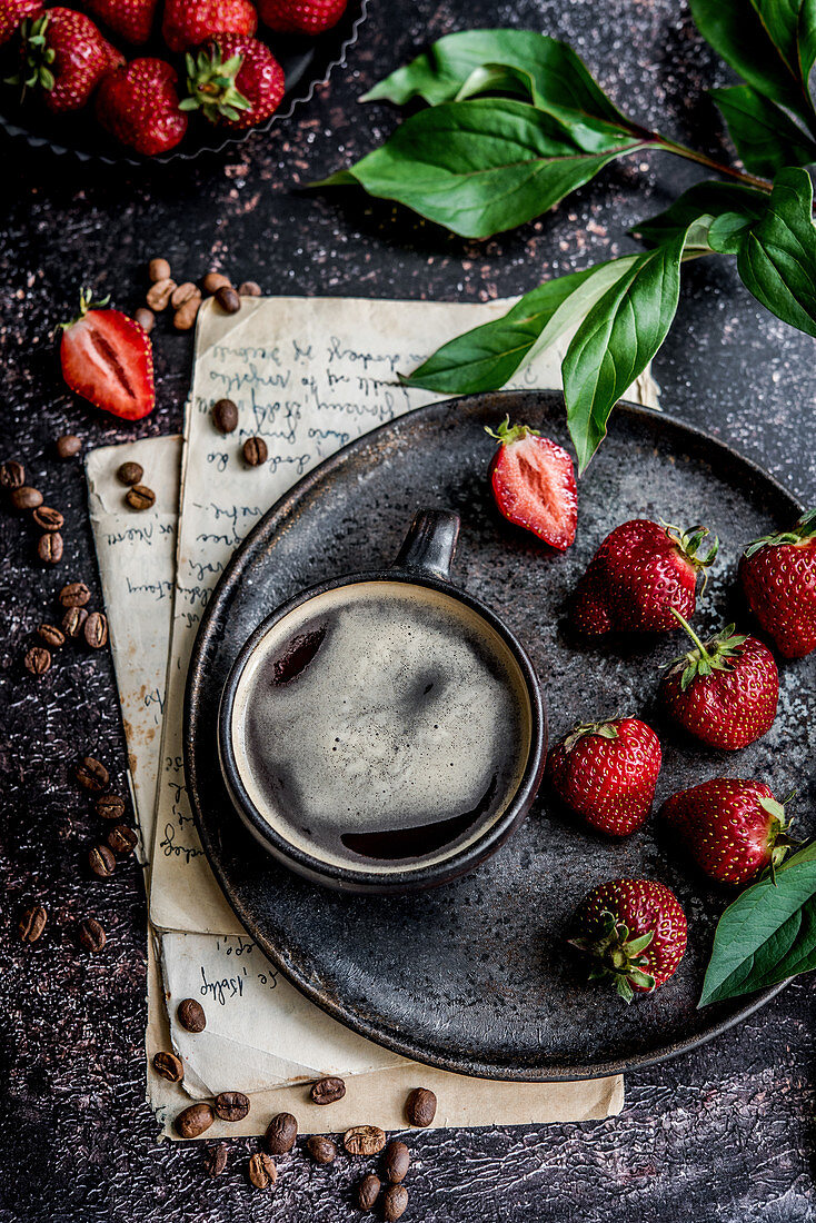 Tasse Kaffee auf Servierteller, daneben Erdbeeren