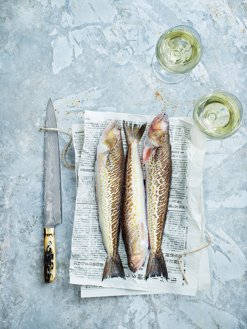 Rohe Fische auf Zeitung, Messer und Weissweingläser