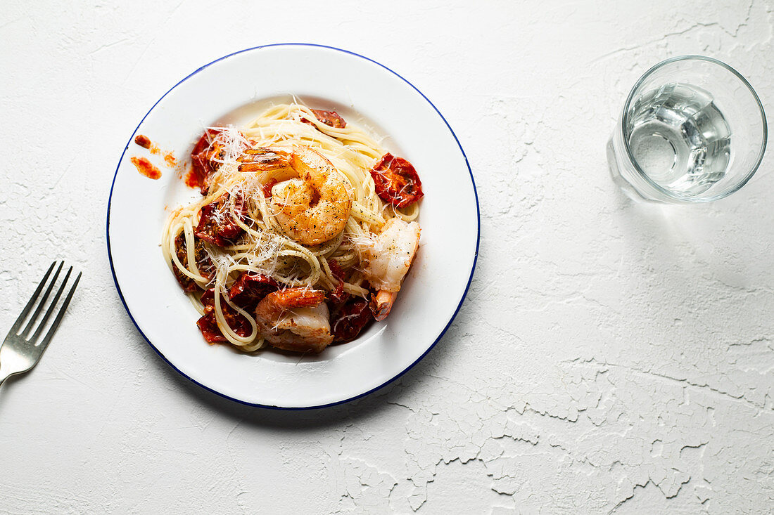Spaghetti with pan seared prawns, oven roasted tomatoes and parmesan, on an enamel plate with a fork