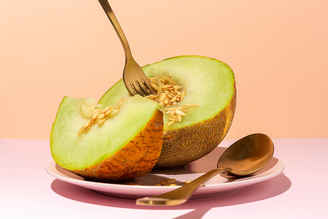 Cut ripe appetizing sweet pitted melon on plate with spoon and fork in pink table