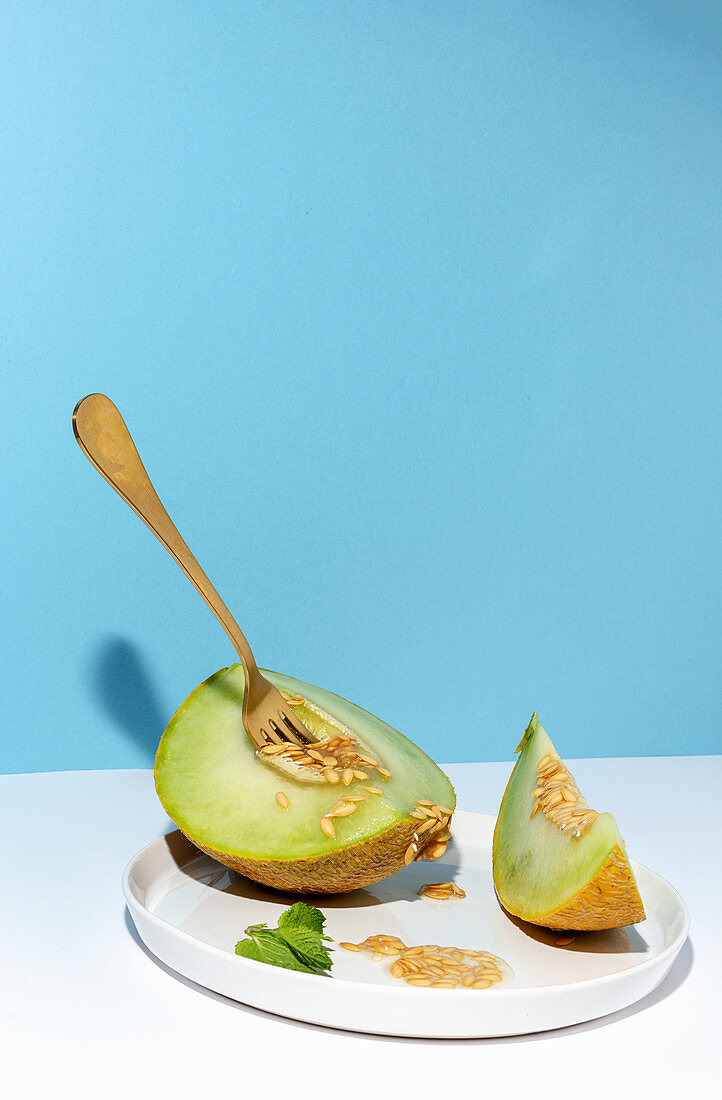 From above cut ripe appetizing sweet pitted melon on plate with spoon and fork in blue table background