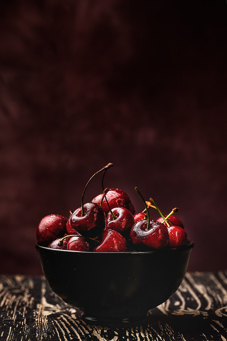 From above tasty appetizing ripe cherry in black brown shining under sunlight on rustic wooden background
