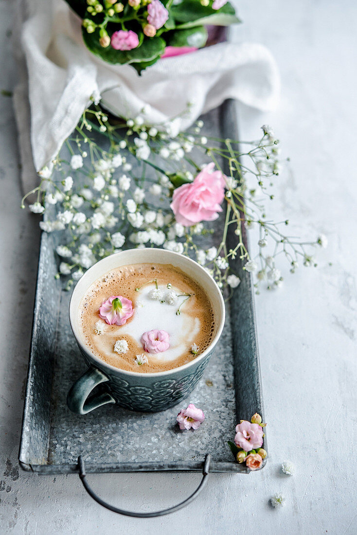 Eine Tasse Kaffee dekoriert mit Milchschaumherz und Blüten