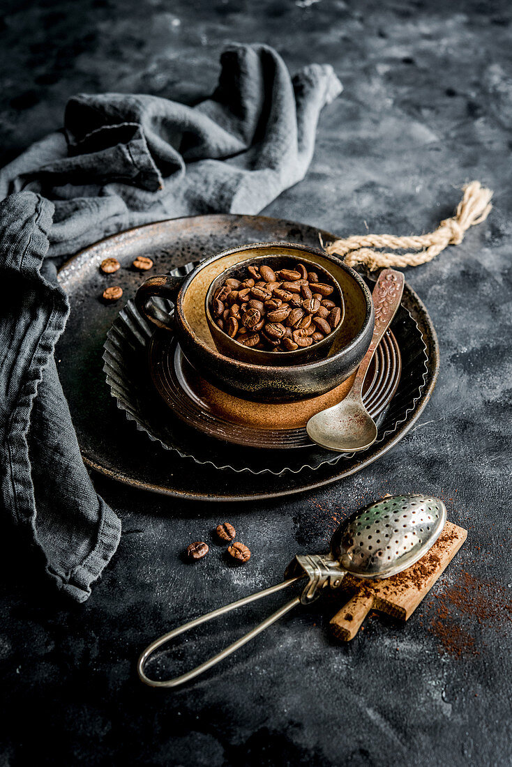Kaffeebohnen im Schälchen, im Vordergrund Sieb mit Kakaopulver