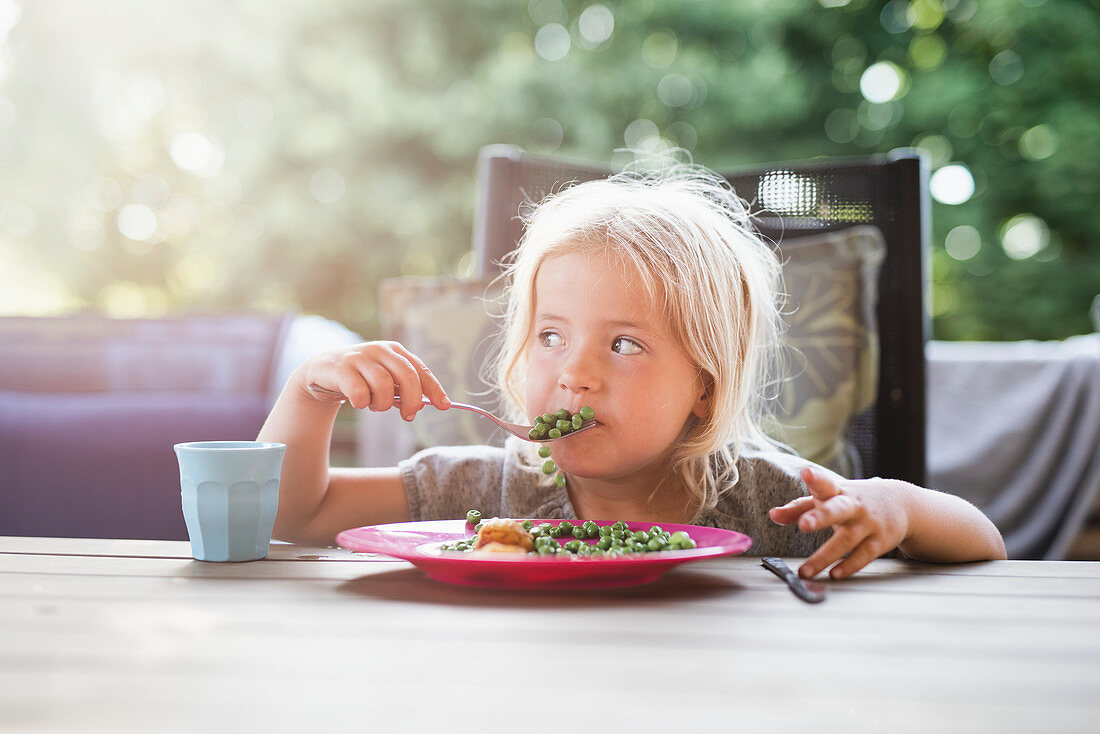 A little girl eating fish and peas on a terrace