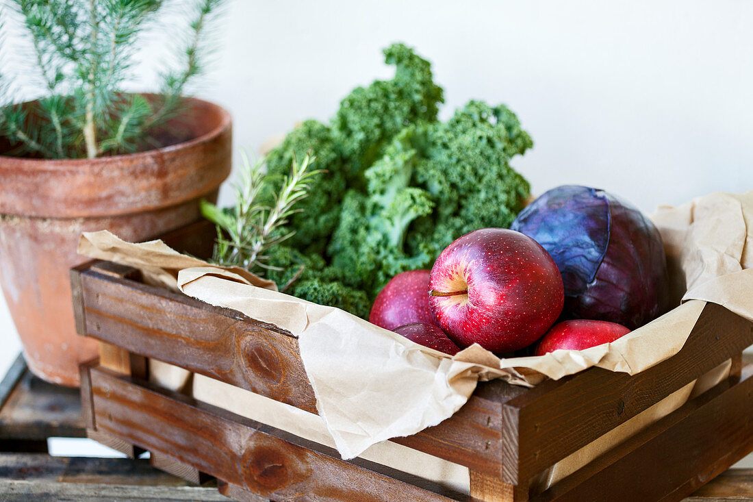 Kale, red cabbage, red apples and rosemary in a wooden crate