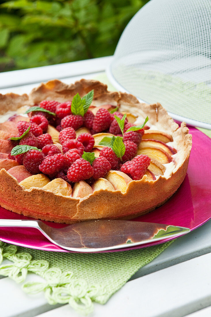 Pfirsichkuchen mit Himbeeren auf Tisch im Freien