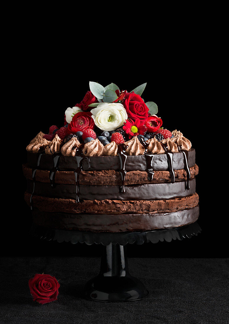 A multi-layer chocolate cake decorated with berries and flowers