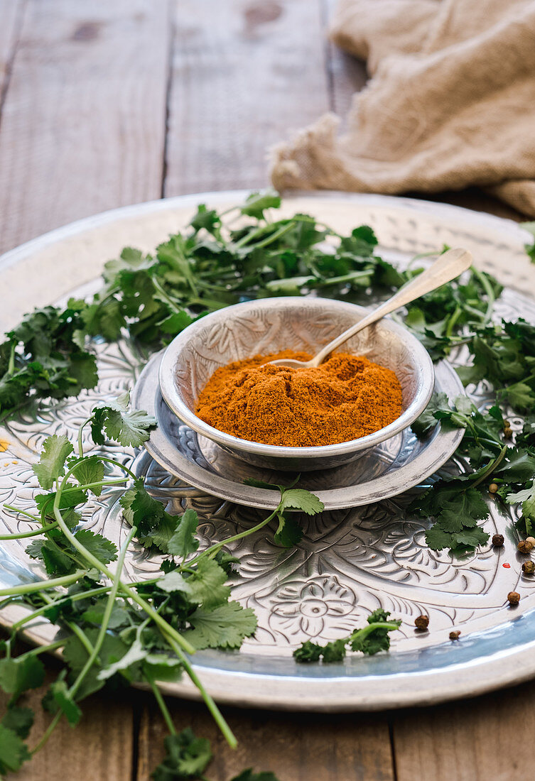 From above friable yellow turmeric in mug and greens on round silver plate on wooden table