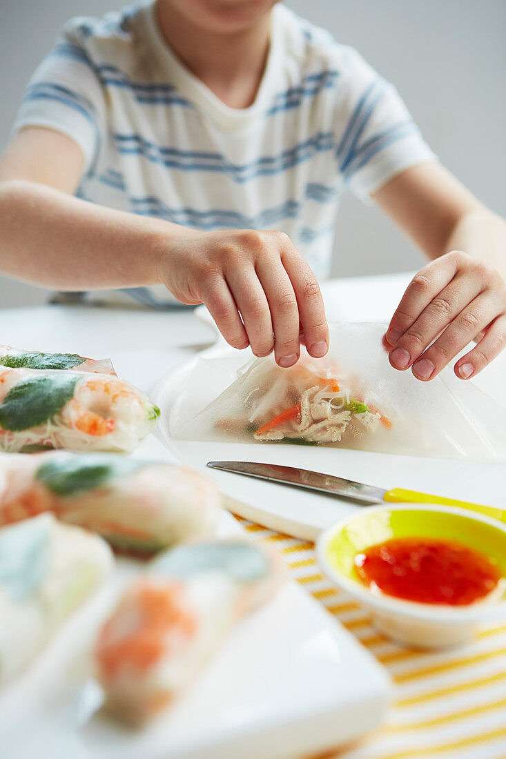 A child preparing rice paper rolls with shrimp filling