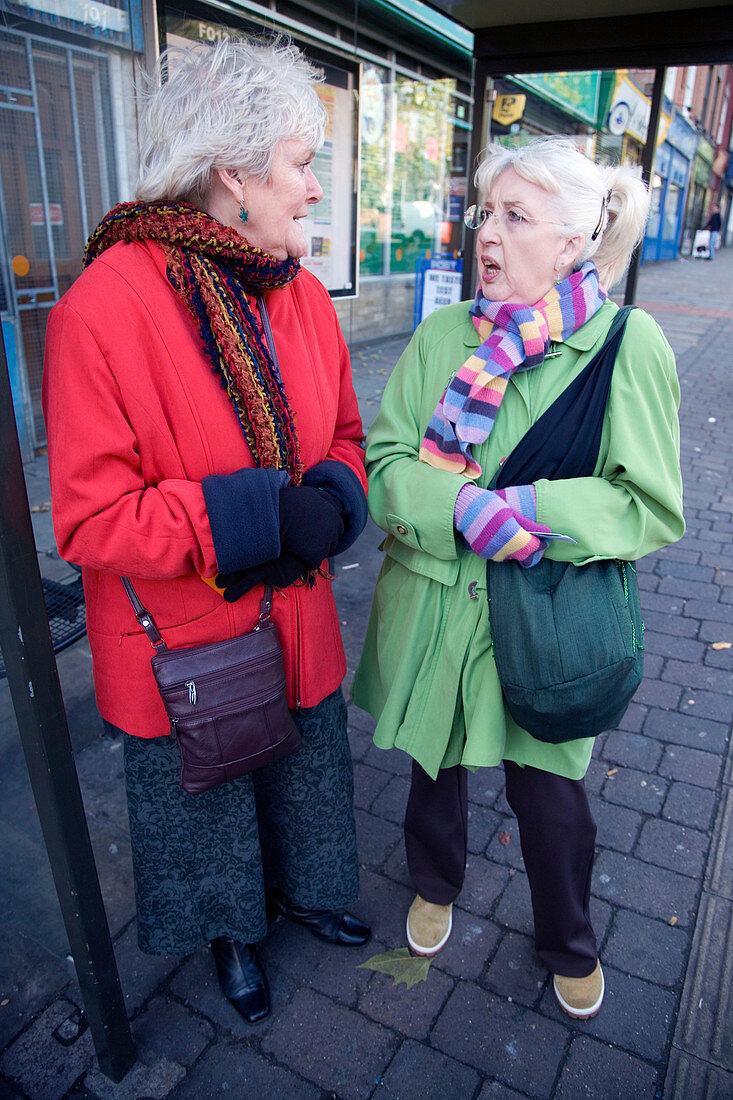 Two friends chatting whilst waiting at the bus stop