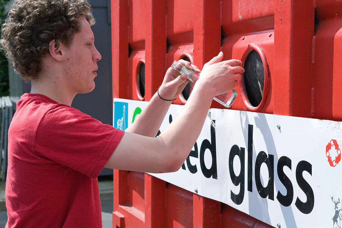 Teenaged boy recycling glass at bottle bank at city tip