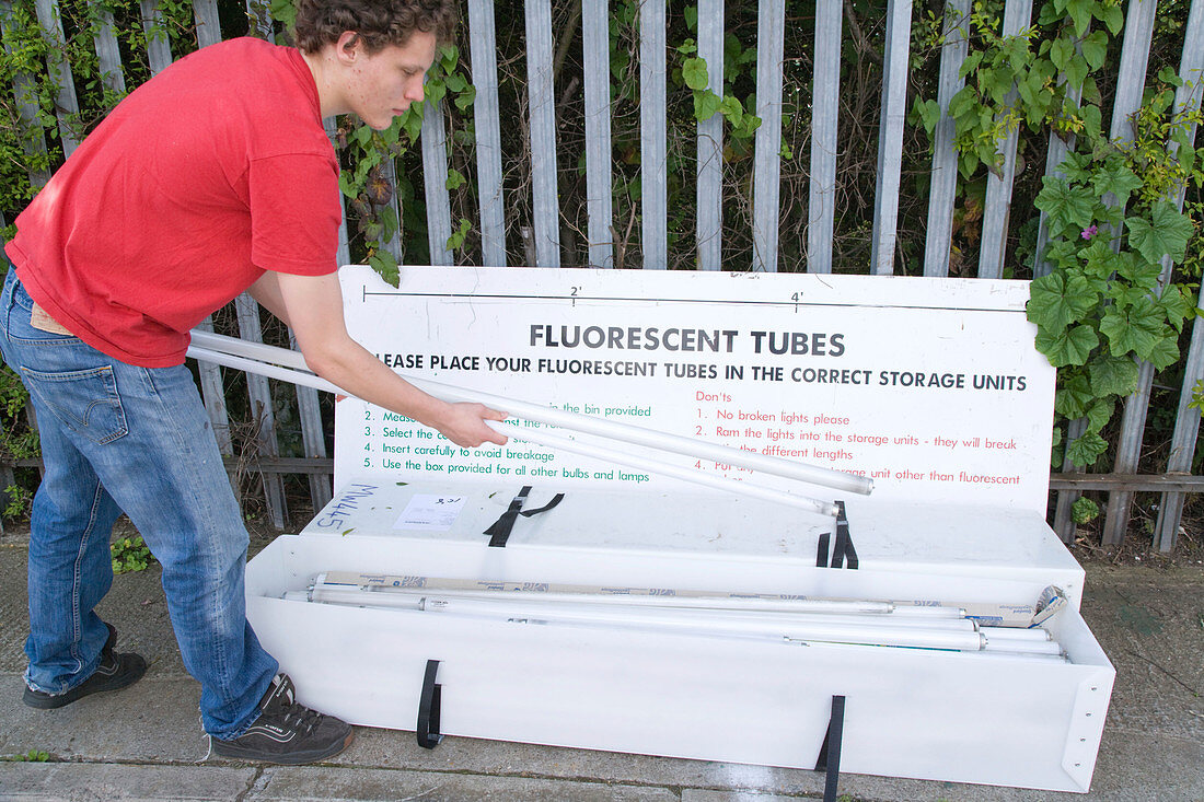 Teenaged boy recycling fluorescent light tubes at city tip