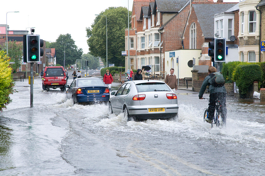 Cars and cyclists drive through flooded street