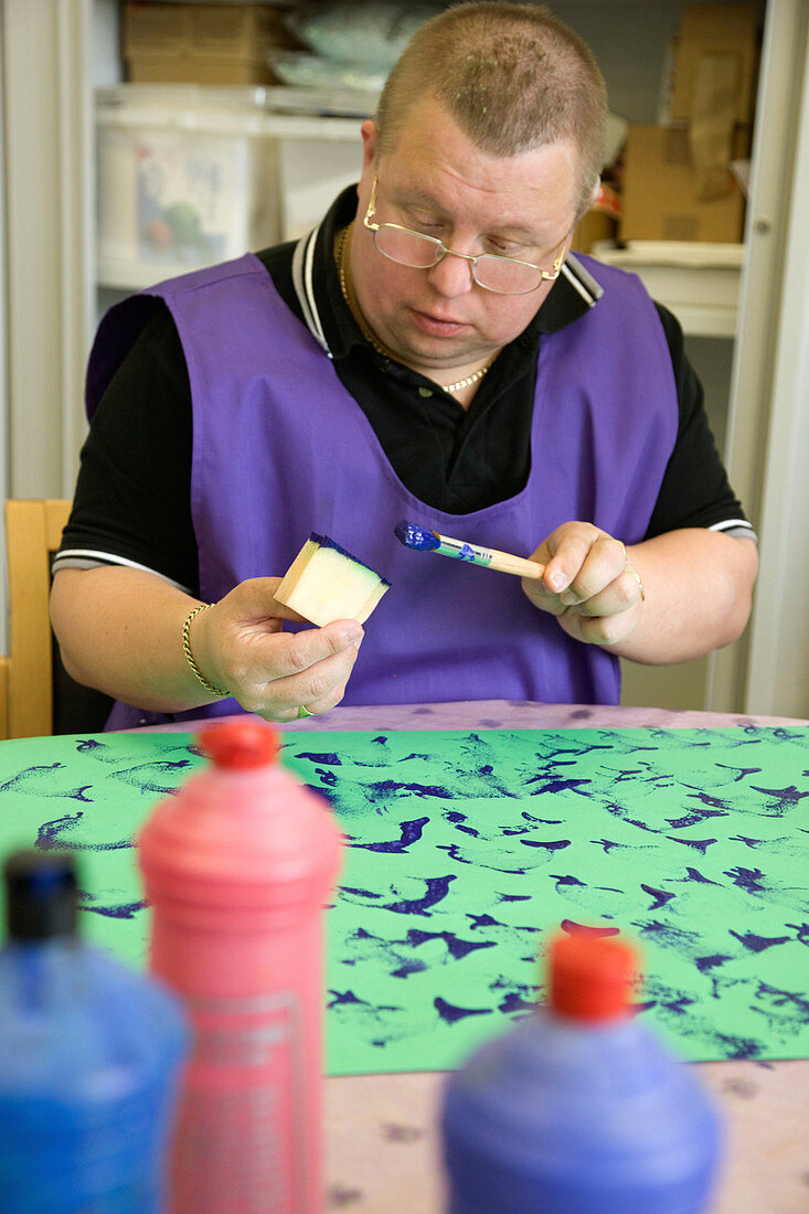 Man with learning disabilities using sponge shapes to paint