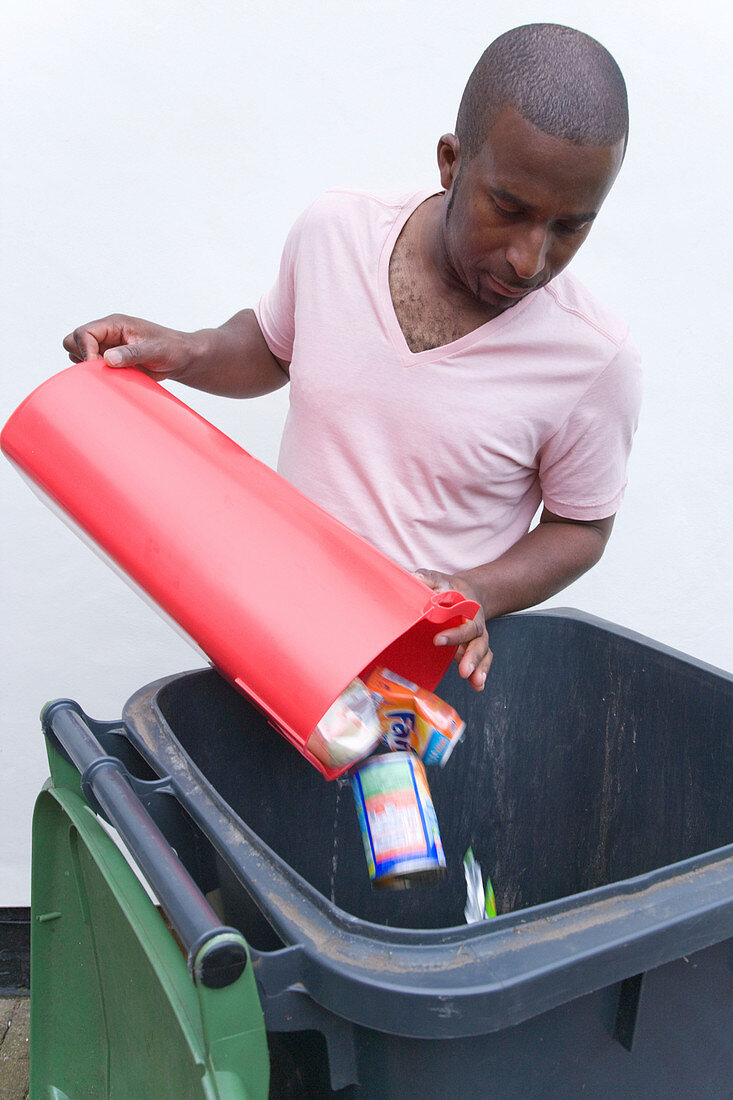 Man putting tins and cans into recycling wheelie bin
