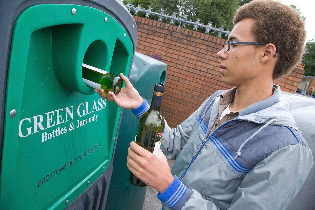 Teenage boy putting bottles into a recycling bank