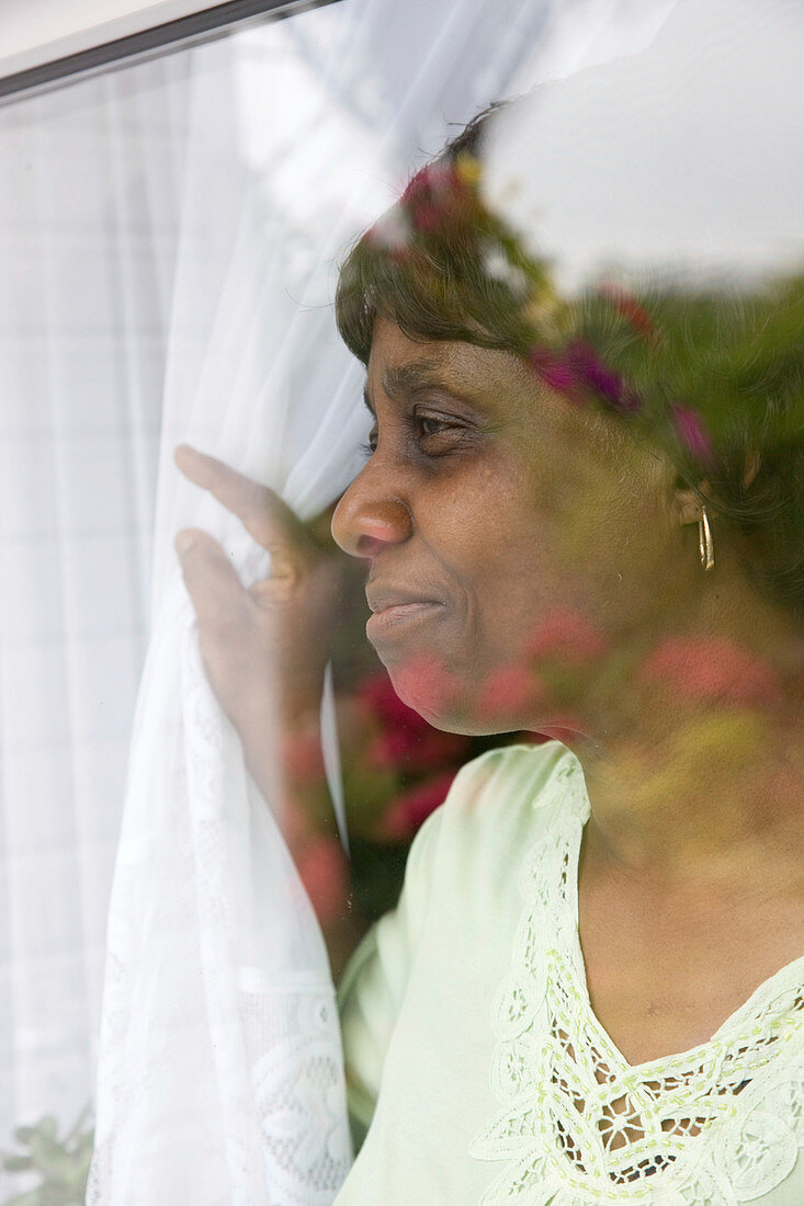 Older woman pulling back her curtain to look out the window