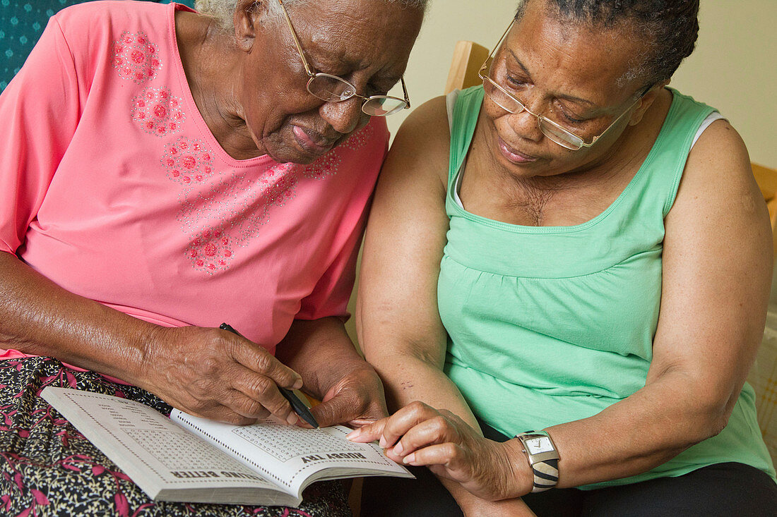 Carer and elderly visually impaired woman solving crossword