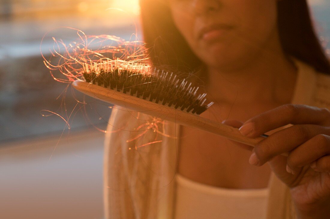 Worried woman holding hairbrush with hair