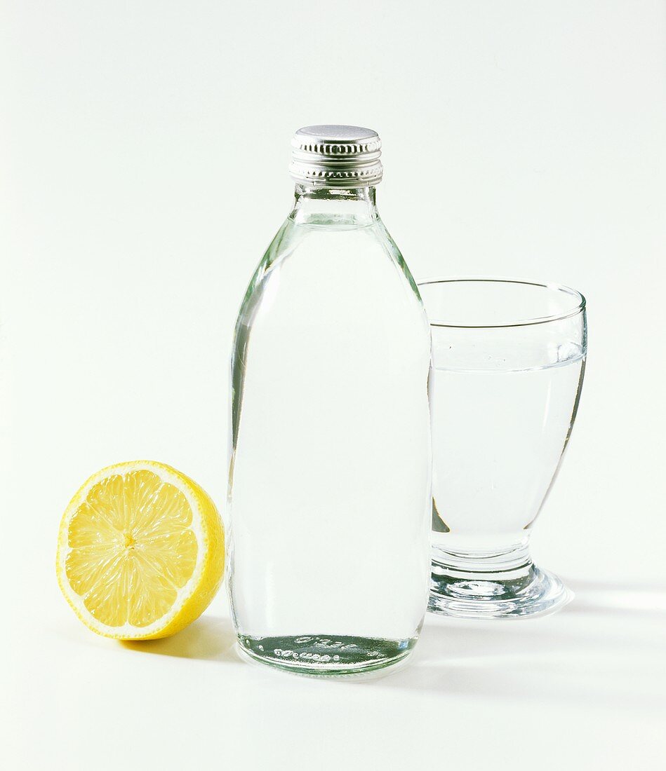 Flasche & Glas mit Mineralwasser & eine halbe Zitrone
