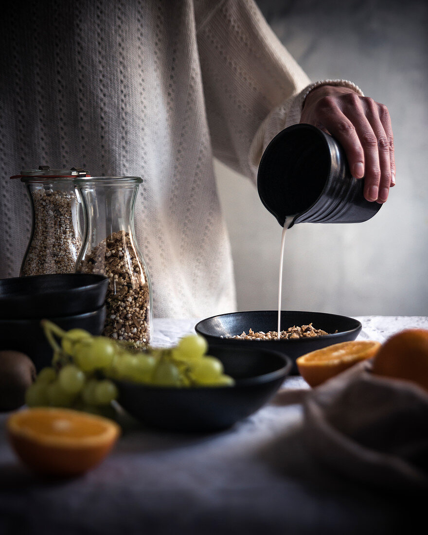 A woman pouring Brazil nut milk into a bowl of muesli