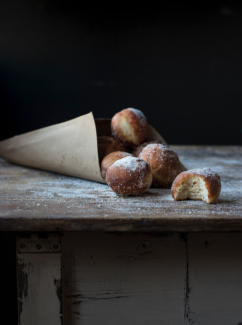 Fresh beignets near set of baked loaf in craft paper with powdered sugar