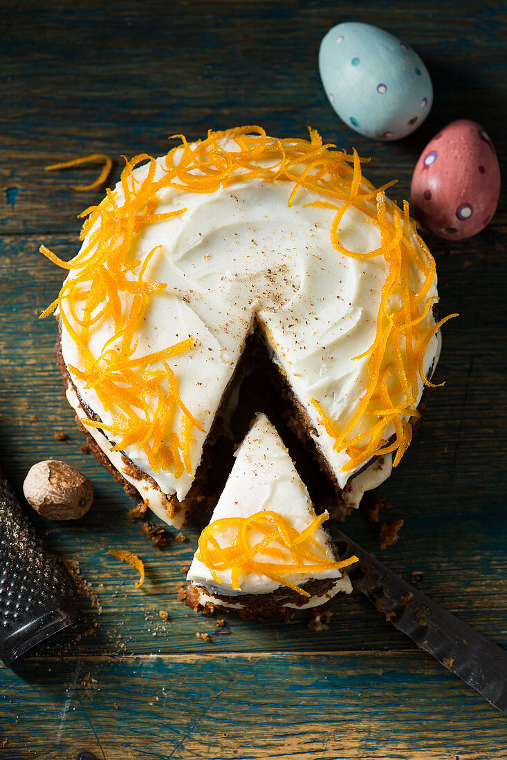 Round carrot cake with a slice cut decorated with candied orange peel