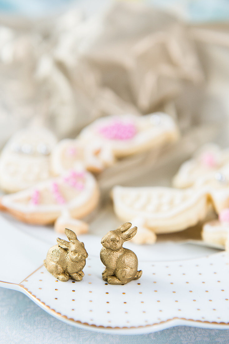Two golden bunnies on plate in front of Easter biscuits