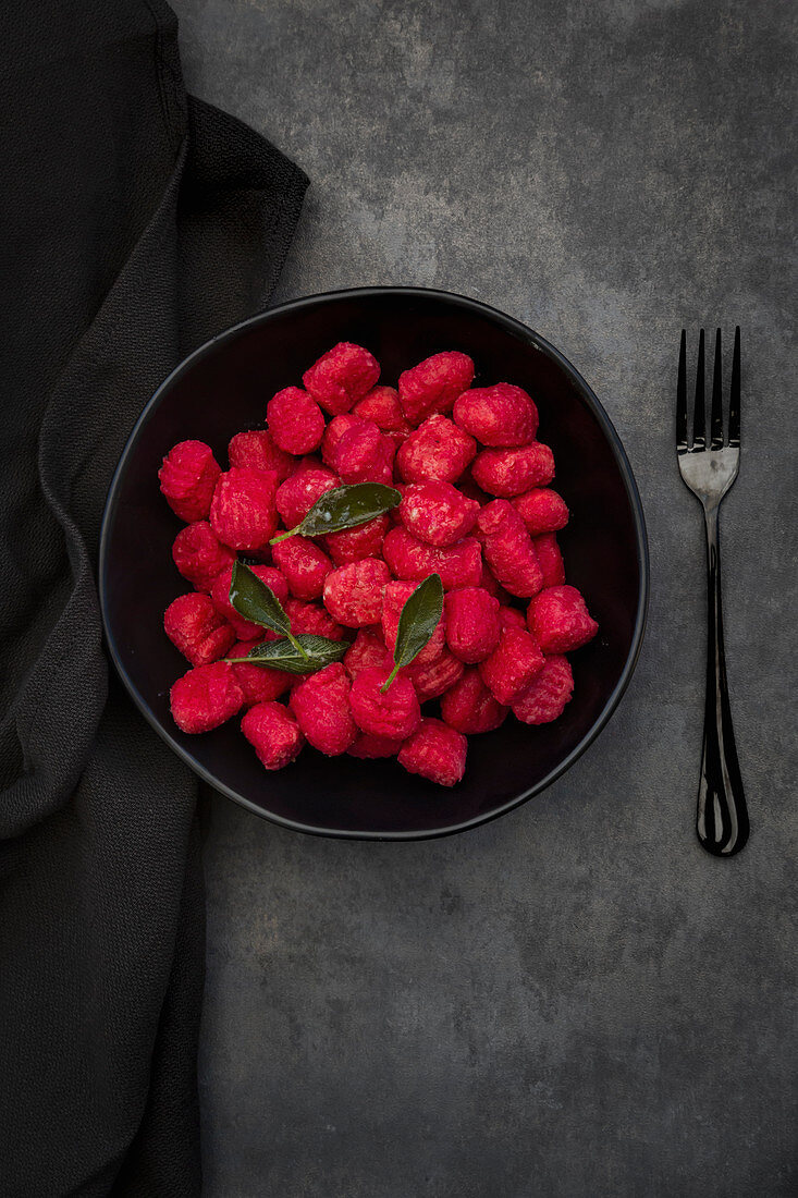 Beetroot gnocchi with sage in a black bowl on a grey surface