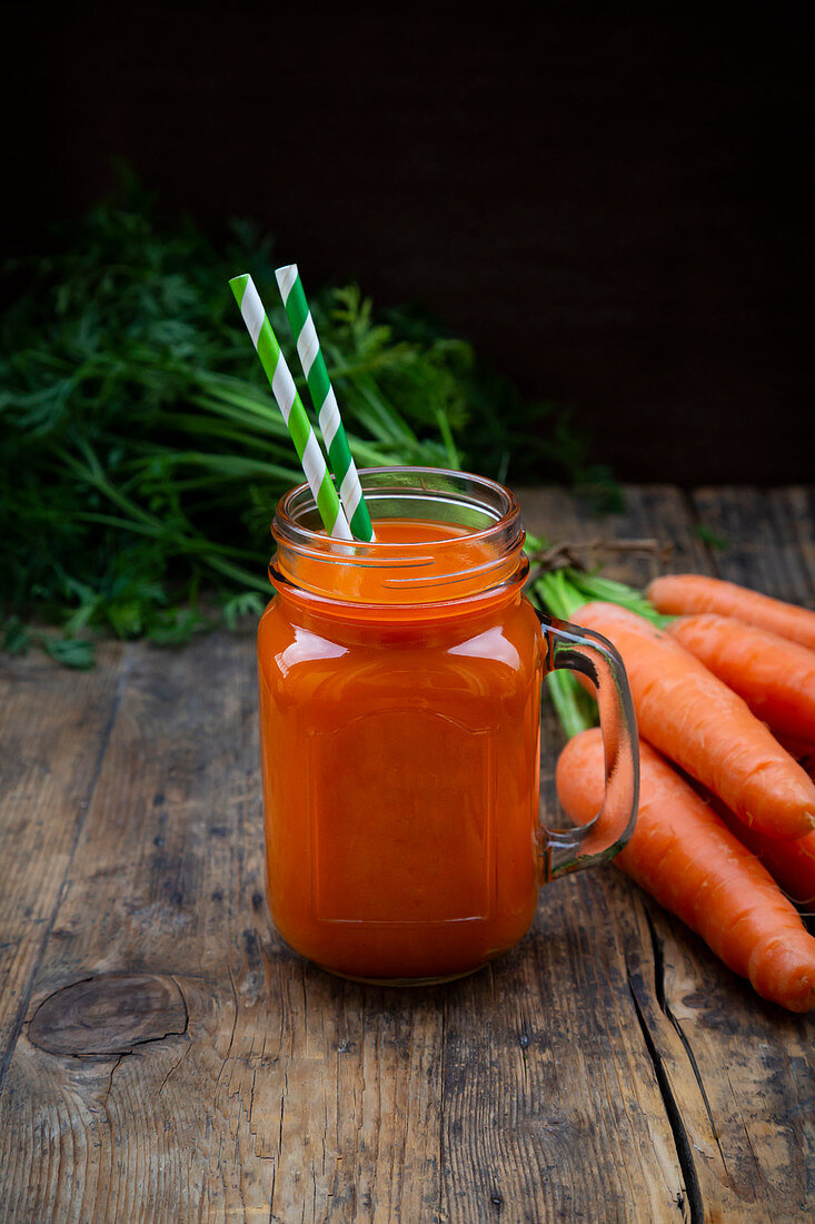 A carrot smoothie with straws in a tankard