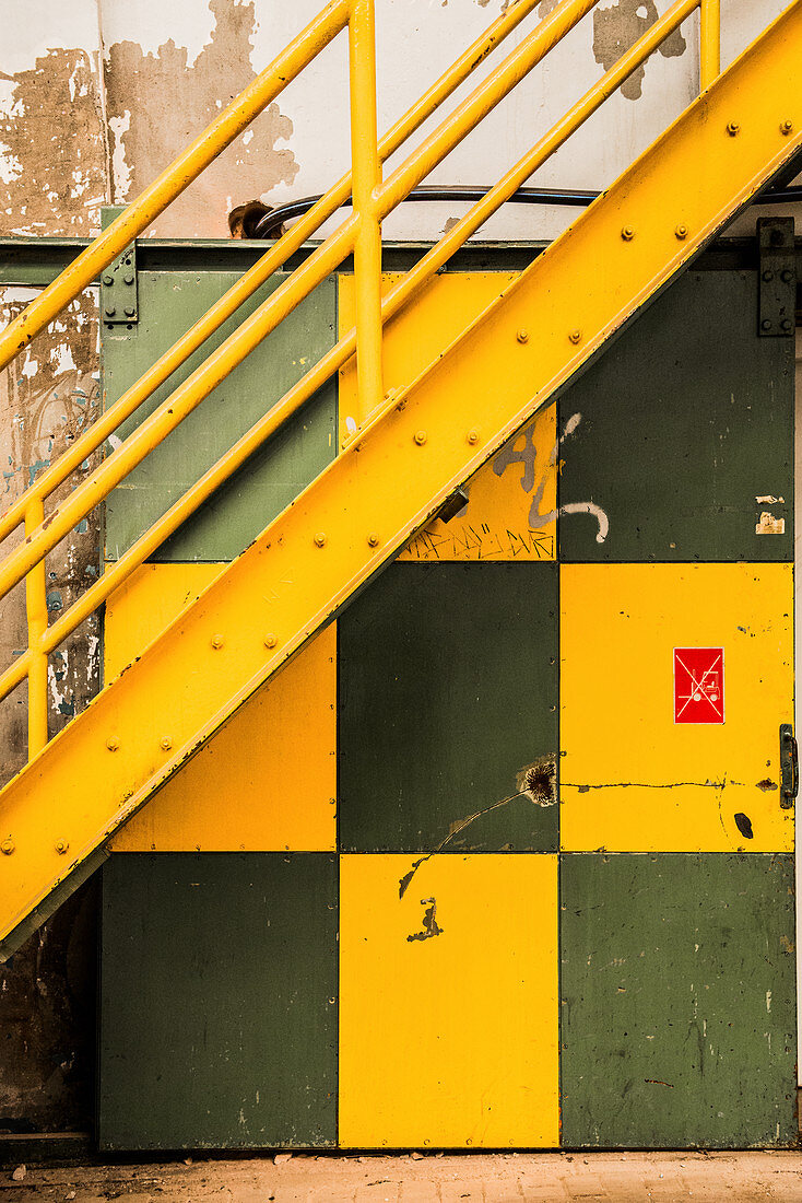 Yellow steel staircase above green and yellow sliding door in factory